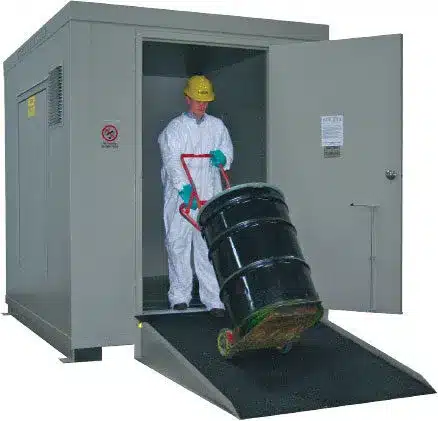 Worker in protective gear moving drums inside a VersaBilt hazmat chemical storage building